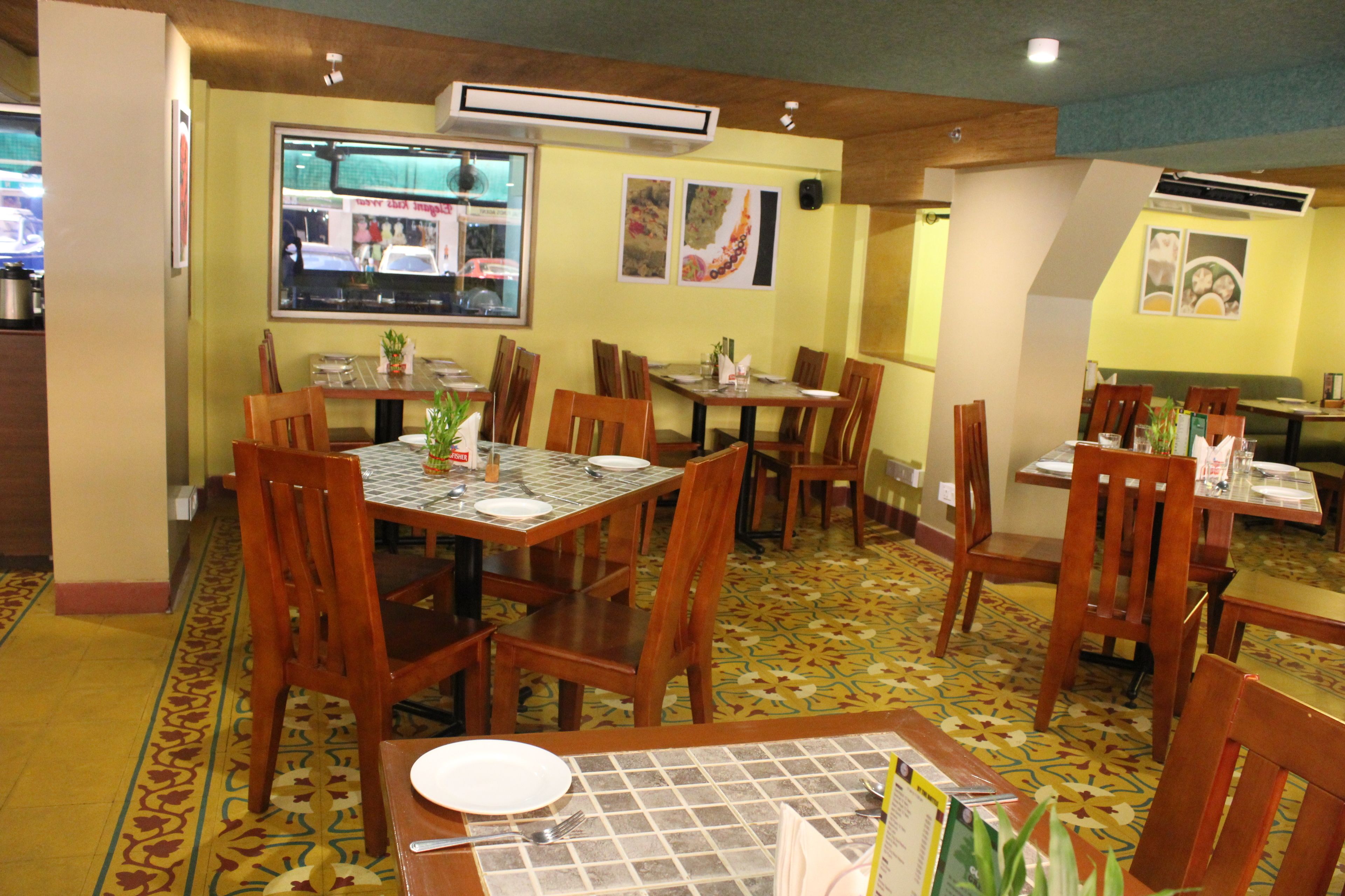 Um restaurante com várias mesas e cadeiras, um piso estampado e uma janela com vista para o exterior.