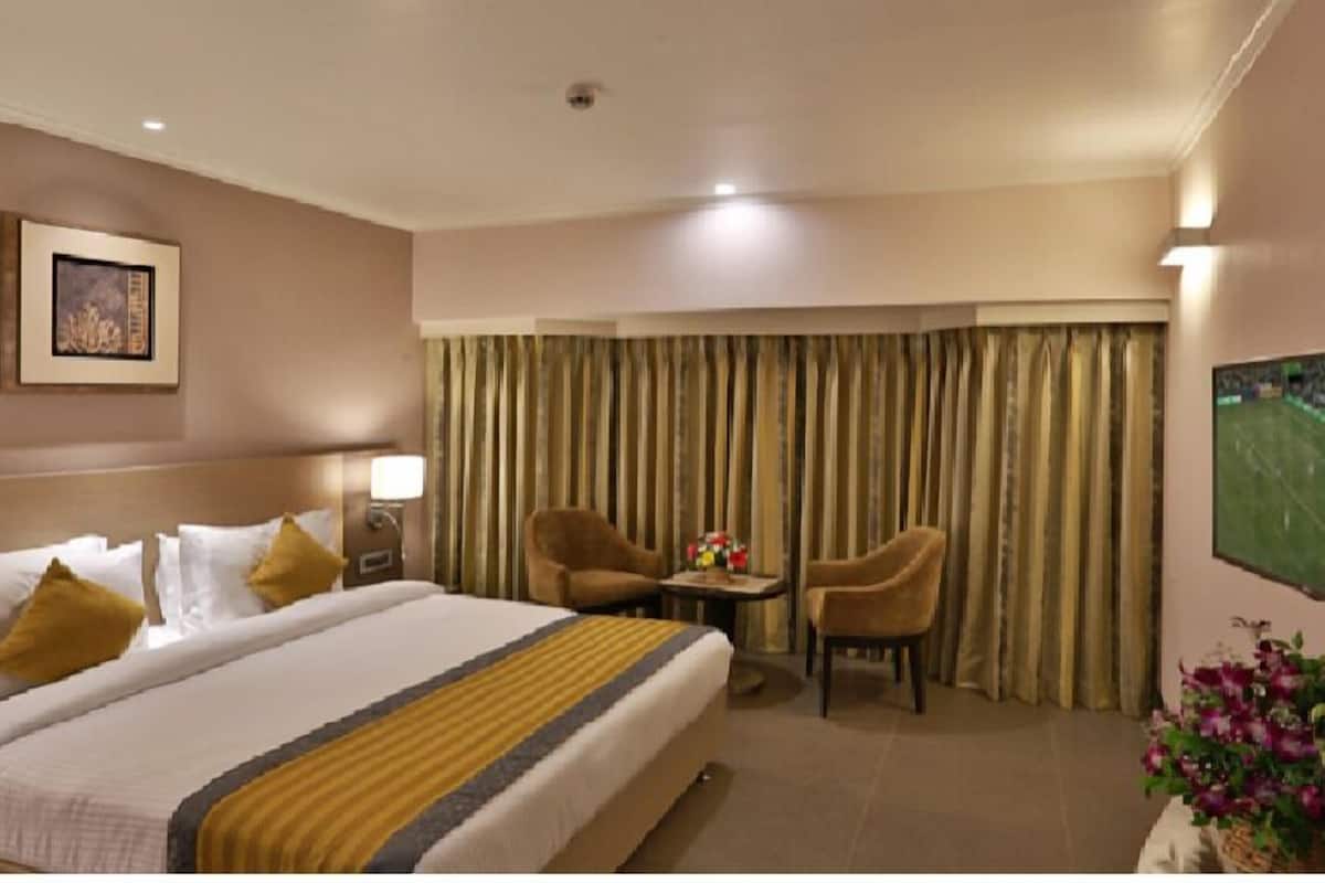 Habitación de hotel con cama, dos sillas, una mesita, lámpara y un cuadro en la pared.