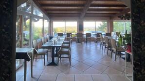 An indoor dining area with a tiled floor, wooden tables and chairs, and large windows allowing natural light. - Les Belles Terrasses (Tourrettes-sur-Loup)