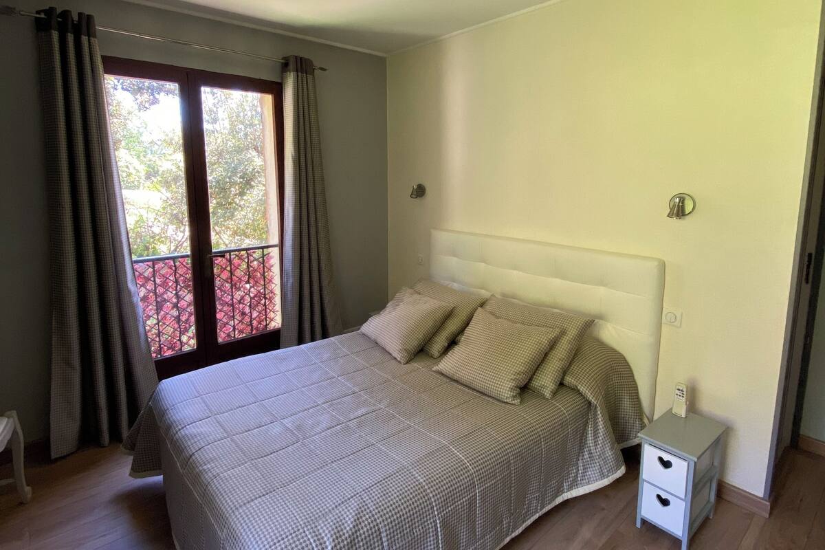 A bedroom with a bed, a nightstand, a ceiling fan, and a window with curtains.