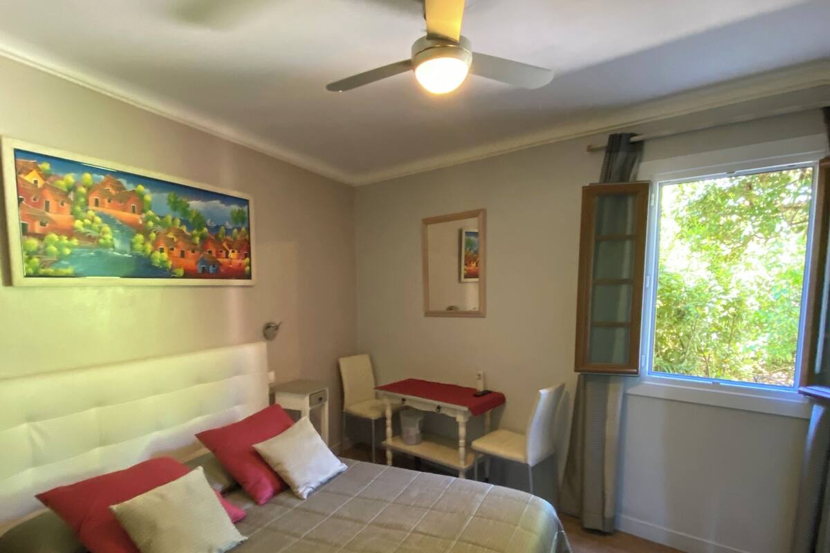 A bedroom with a bed, a desk, a chair, a ceiling fan, and a window with curtains.