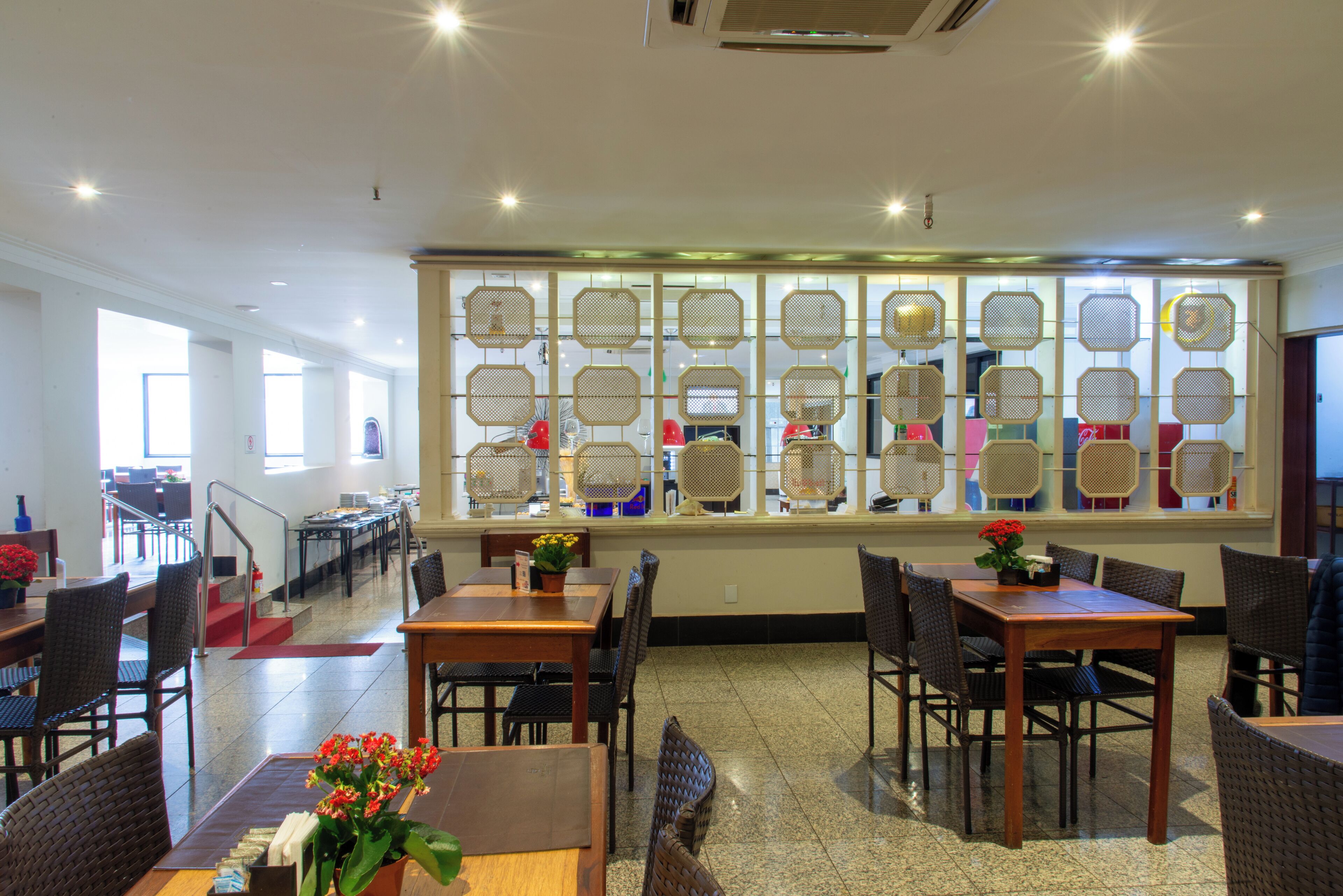 A spacious dining area with multiple tables and chairs, a staircase leading to another level, and a decorative wall with geometric patterns.