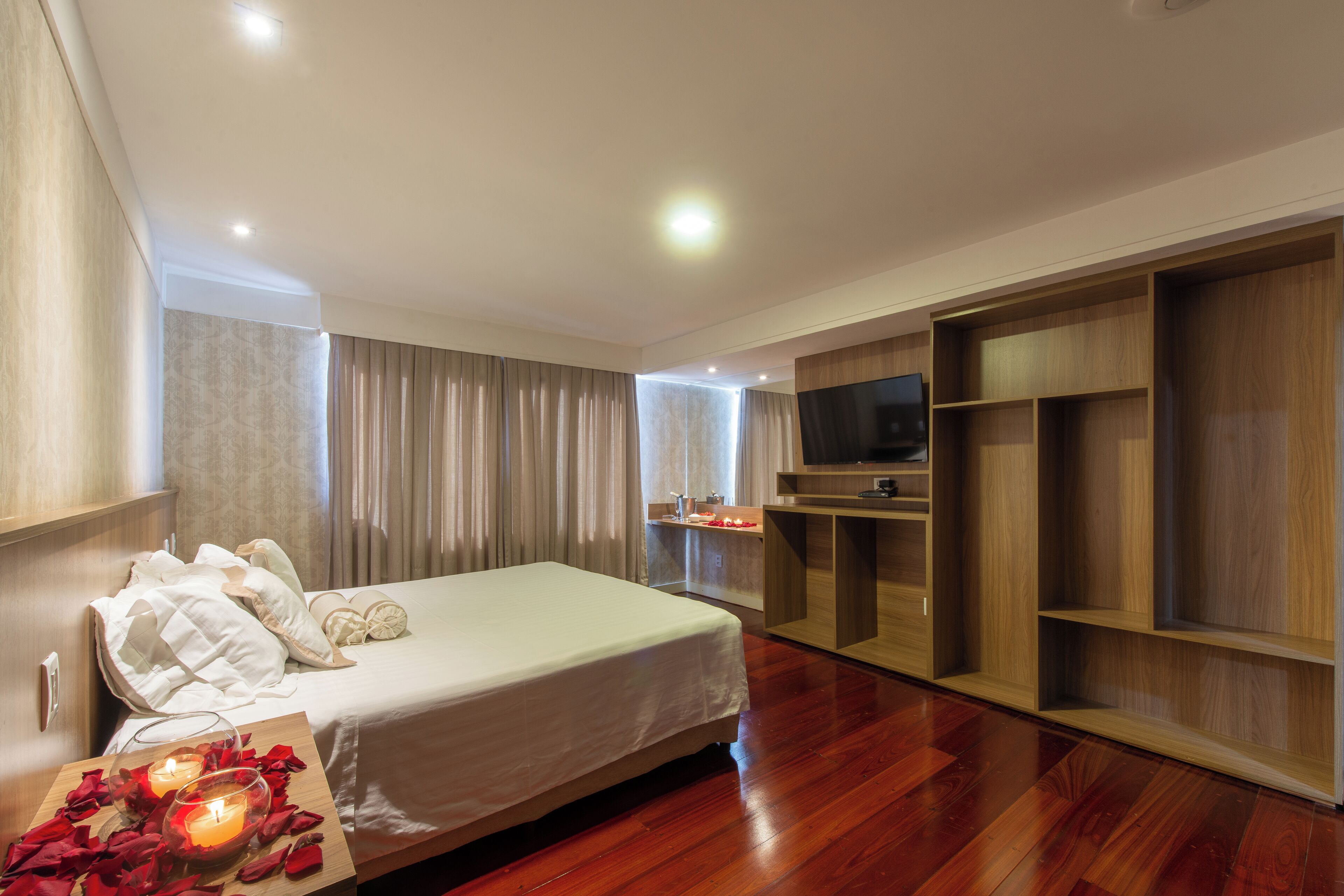 A modern hotel room with a large bed, wooden wardrobe, and a TV on a wooden shelf.