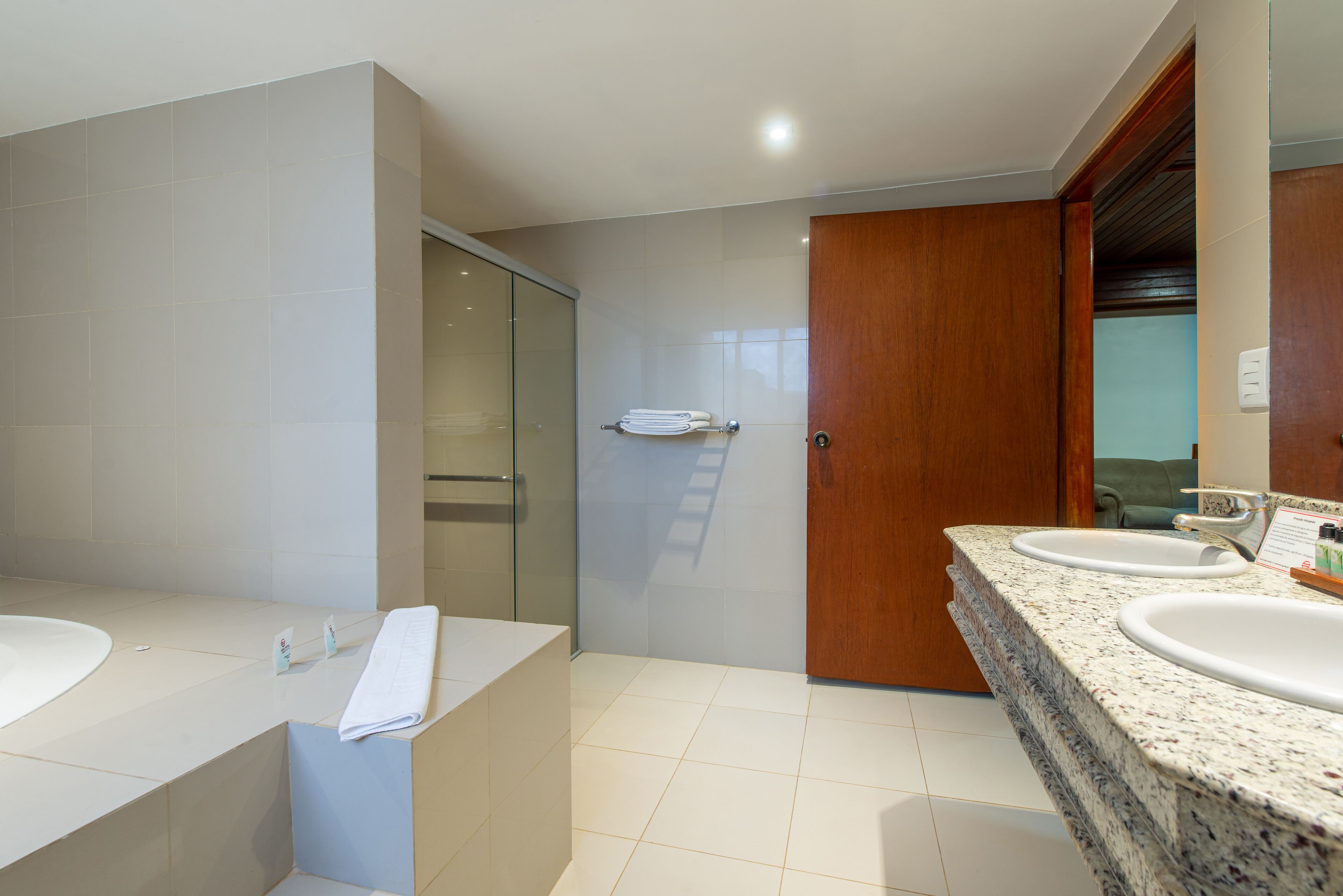 A modern bathroom with two sinks, a glass shower enclosure, and a wooden door.