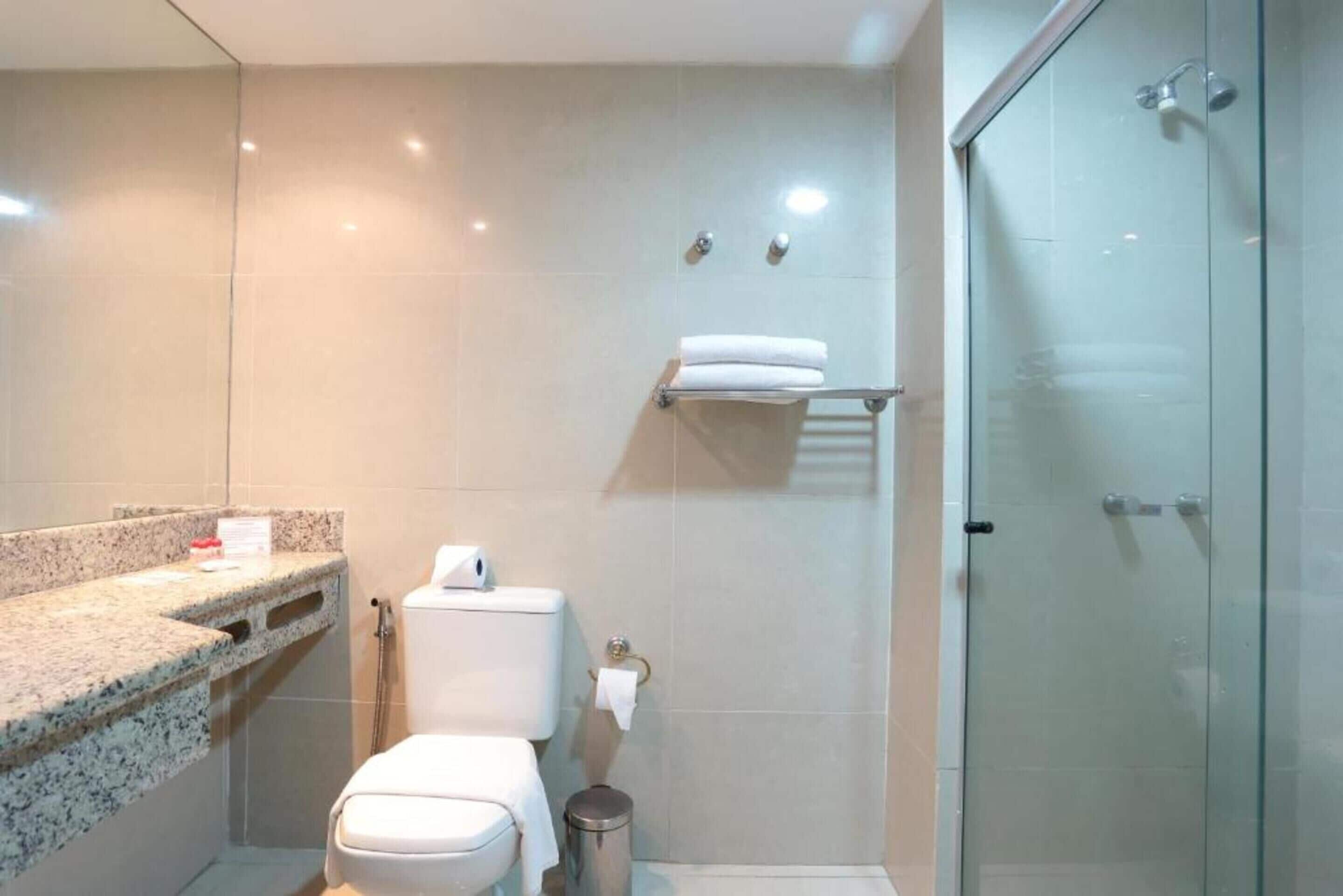Un baño moderno con encimera de granito, inodoro, cabina de ducha con mampara de vidrio y un perchero para toallas.