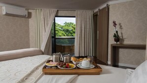 A hotel room with a bed, a breakfast tray with food and drinks, a window with curtains, and an air conditioning unit. - Taiwan Hotel (Ribeirão Preto)