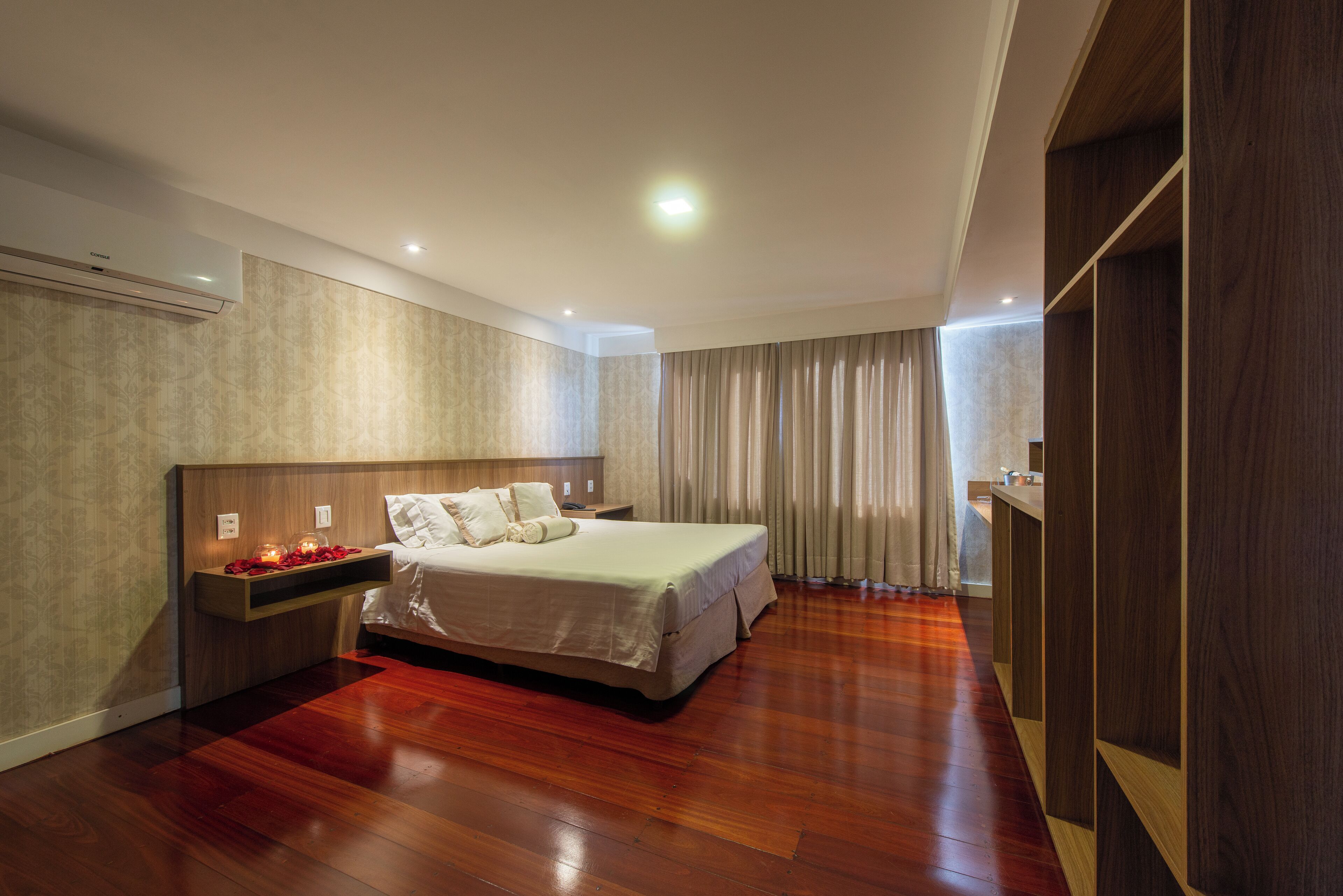A modern bedroom with a large bed, bedside tables, a built-in wardrobe, and an air conditioning unit.