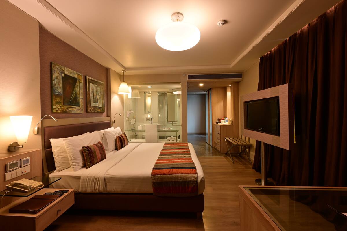 A hotel room with a large bed, bedside table with a phone and lamp, a TV, and artwork on the wall.