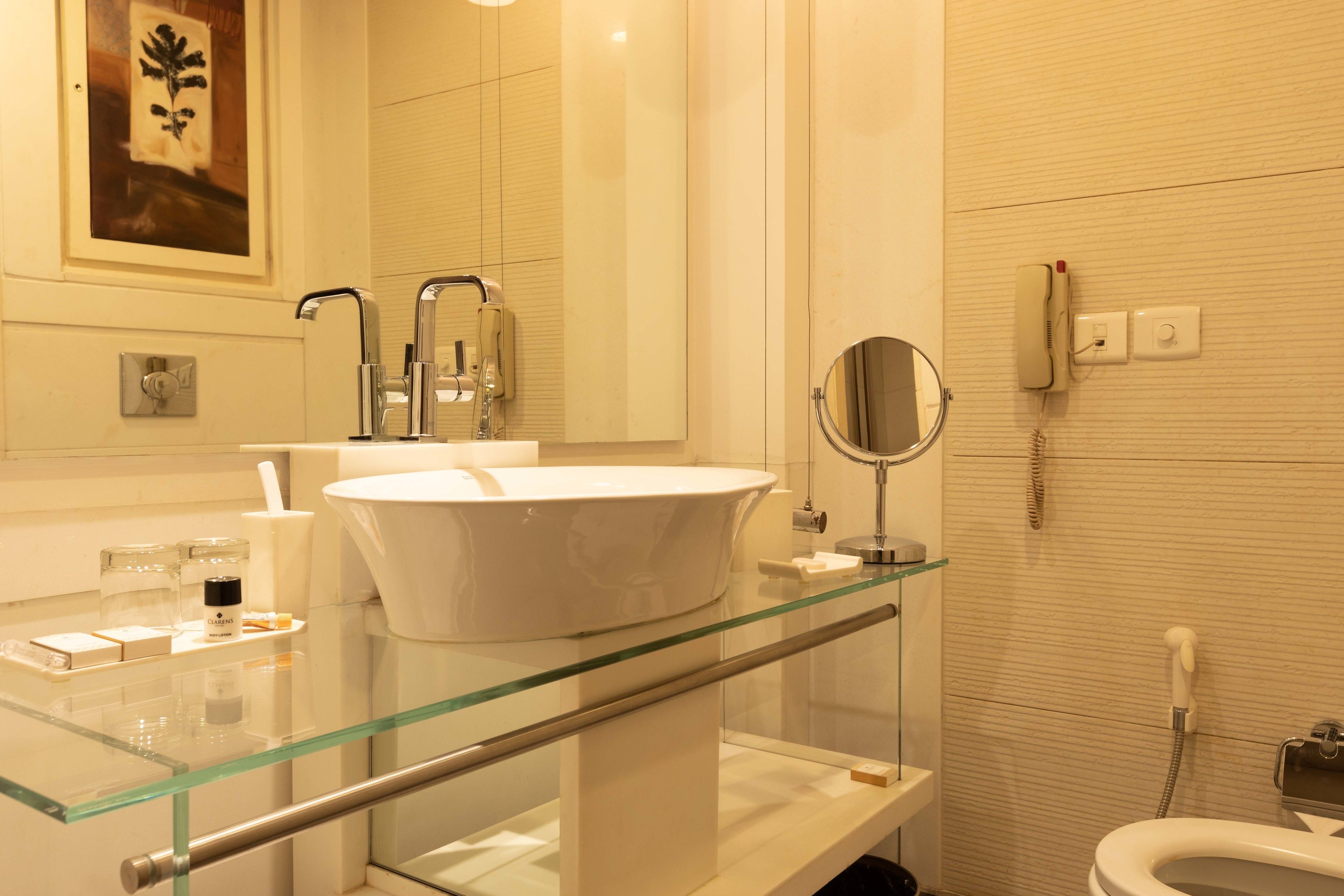 A modern bathroom with a glass-enclosed sink, a handheld mirror, and a telephone.