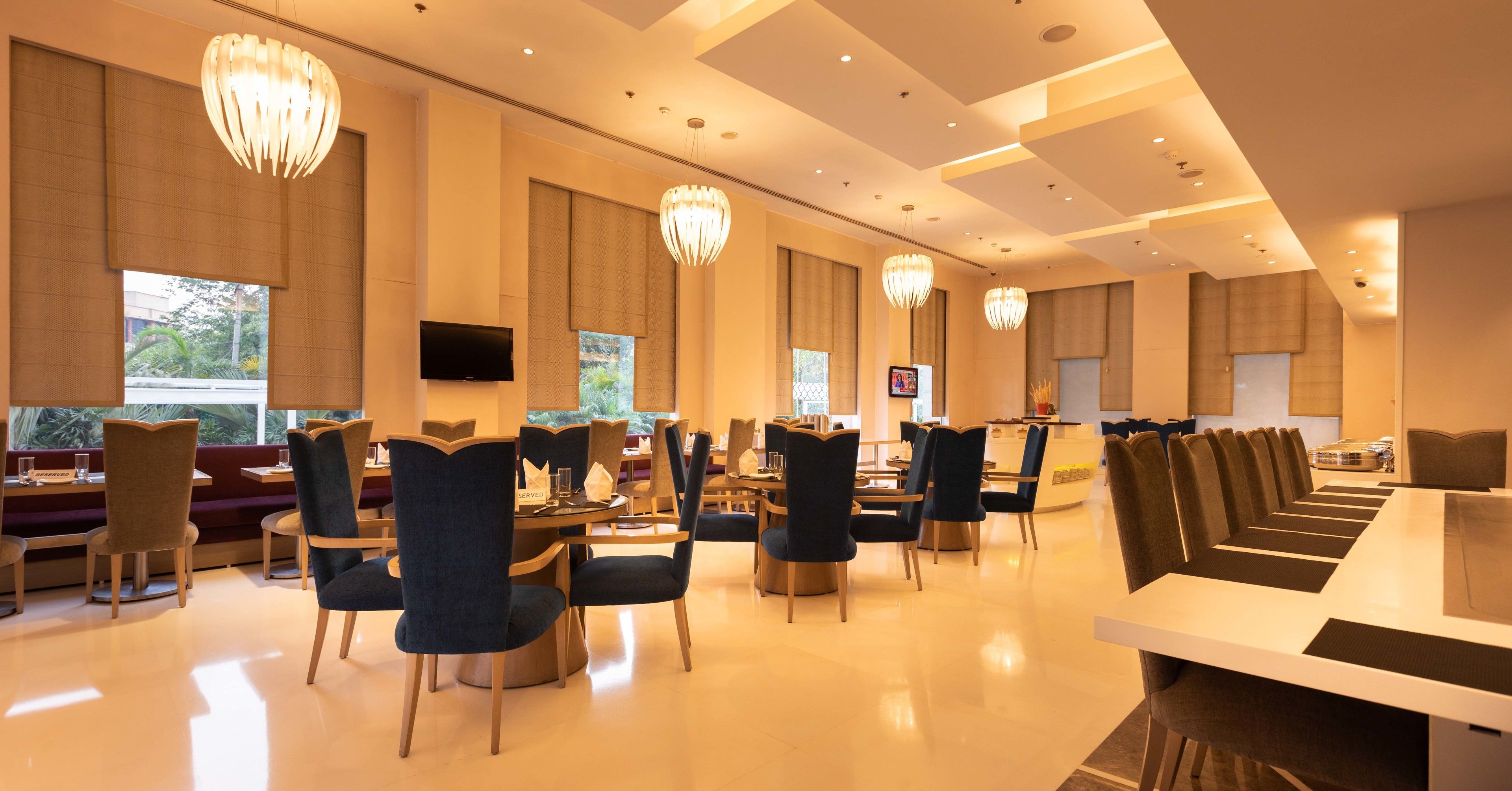 A spacious restaurant with high ceilings, modern chandeliers, and a variety of seating arrangements including booths and tables.
