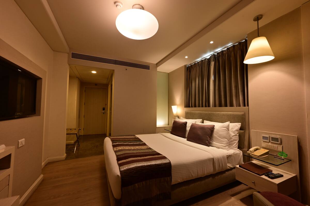 A hotel room with a large bed, bedside table with a lamp, a TV, and a desk with a telephone.