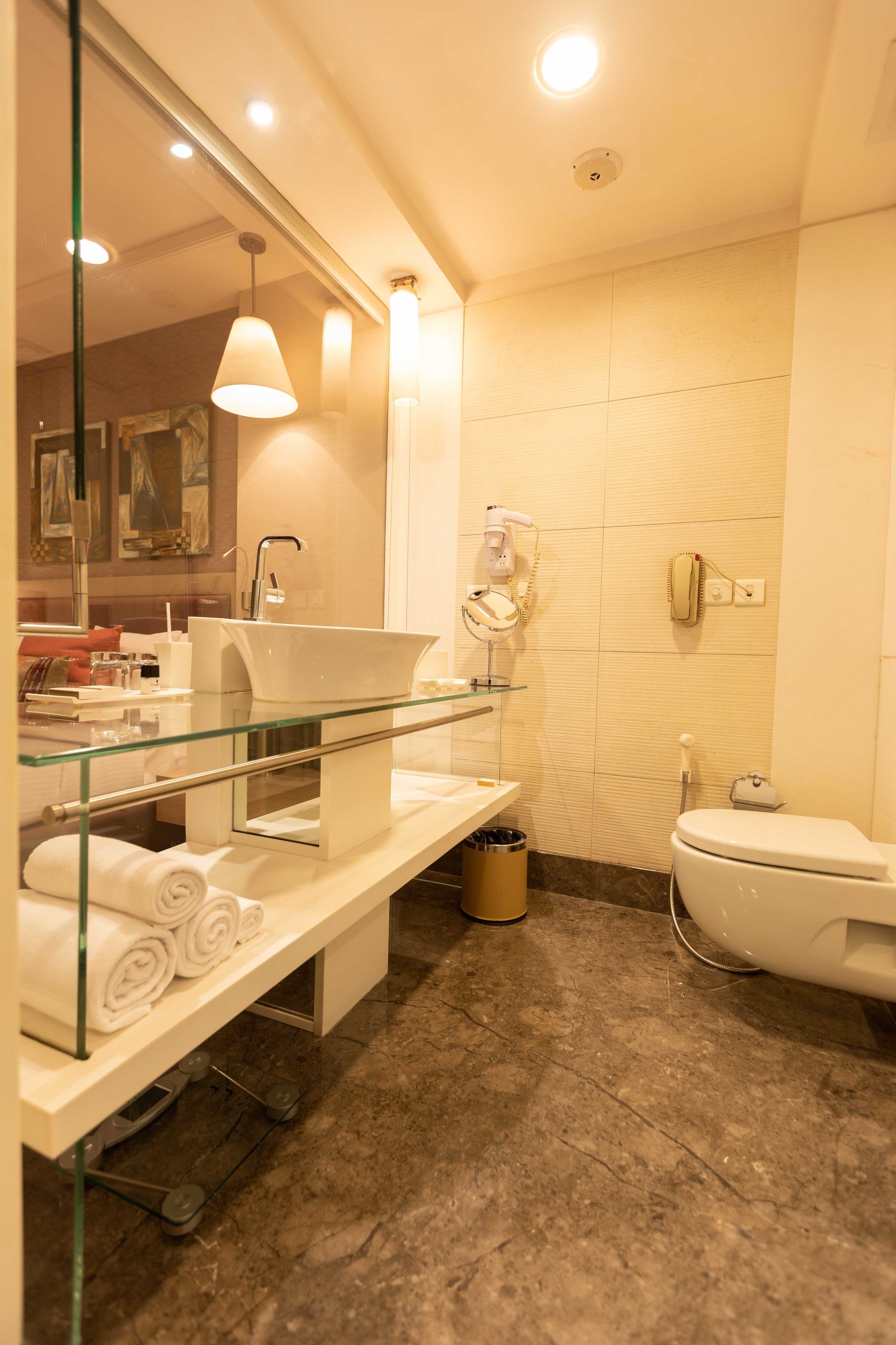 Un baño moderno con lavamanos con cerramiento de vidrio, inodoro y secador de pelo en un estante de pared.