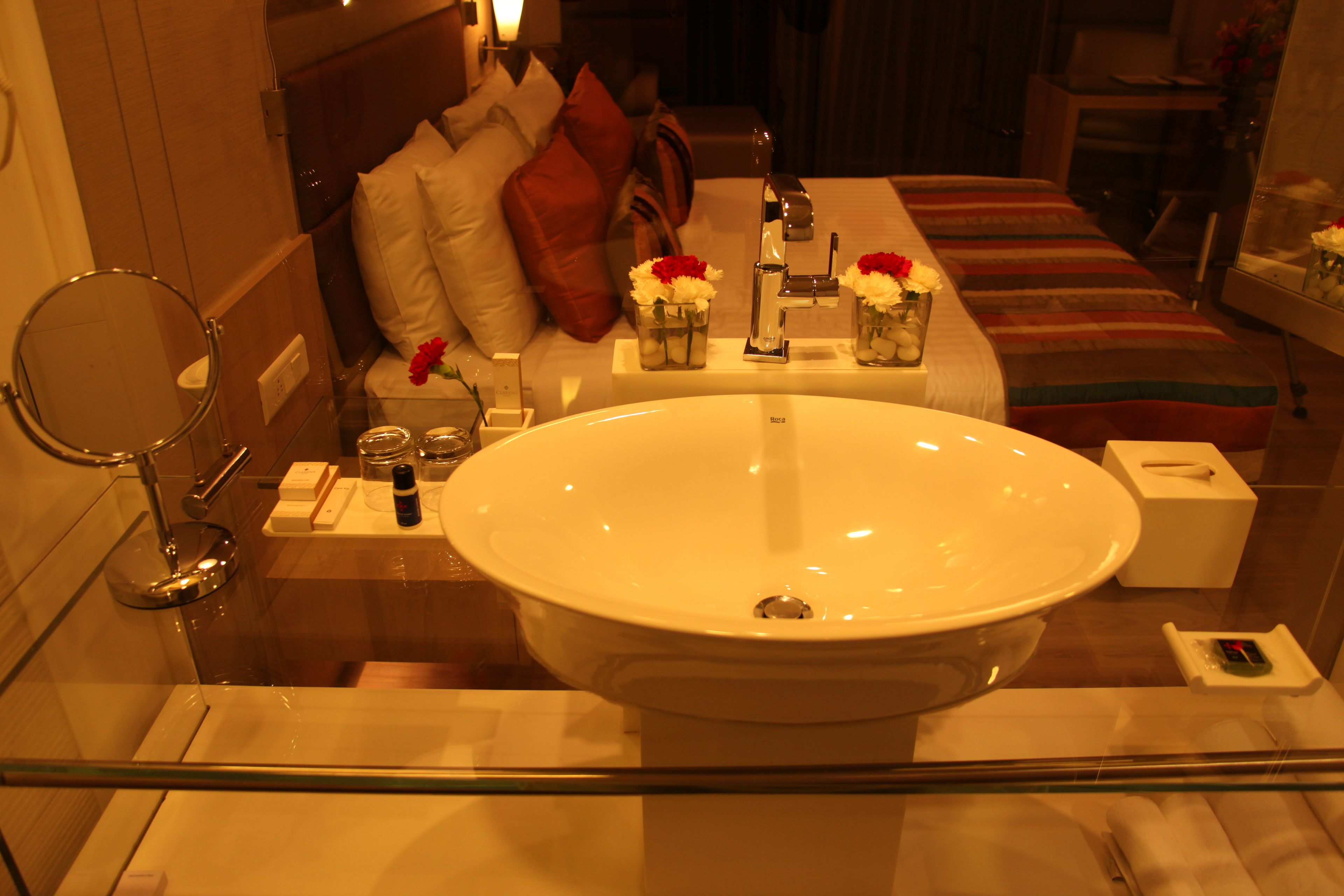 Une salle de bain avec un grand lavabo blanc, un miroir et un lit avec des oreillers et une couverture à rayures.