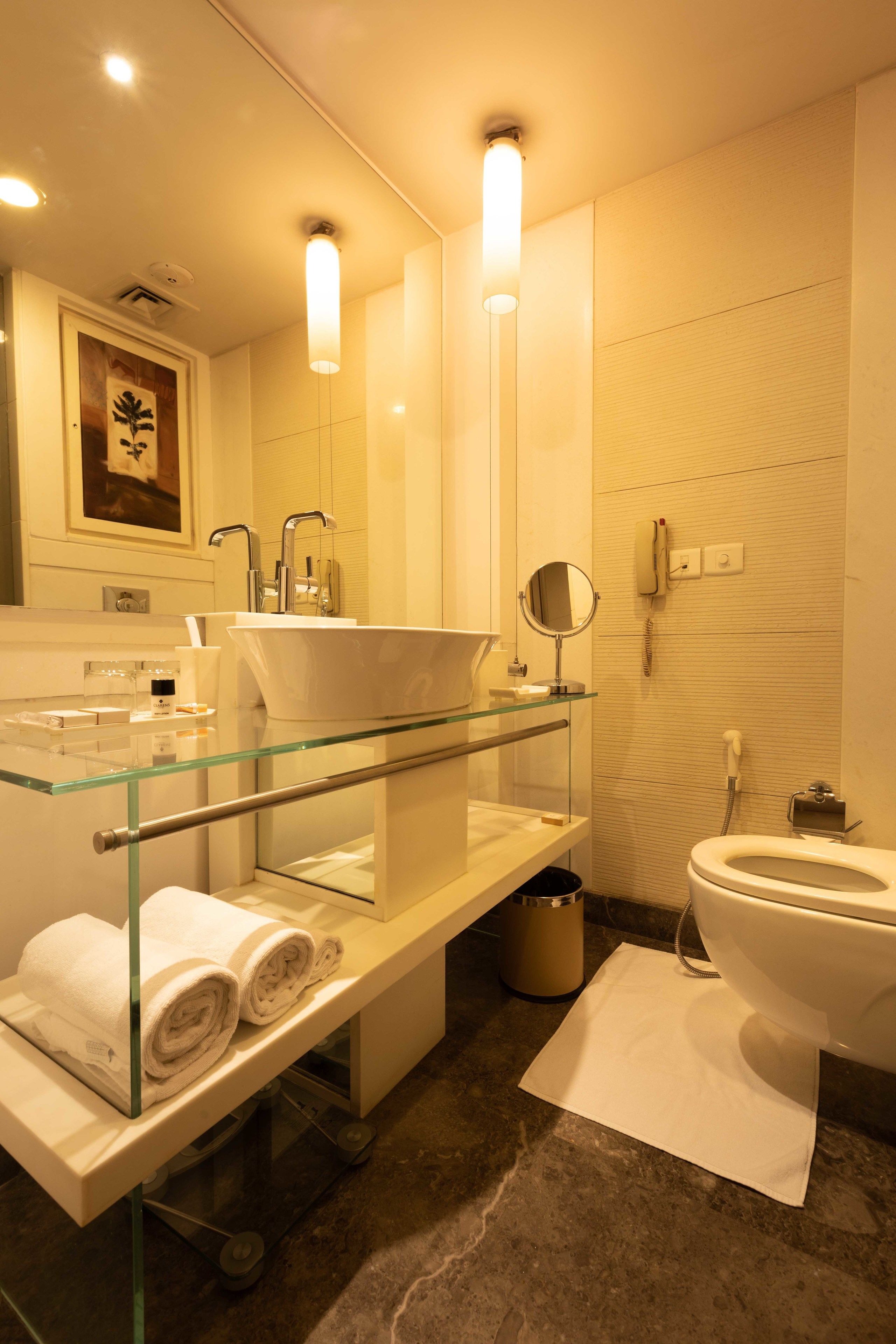 Un baño moderno con tocador de vidrio, un lavamanos blanco, un inodoro y un espejo.