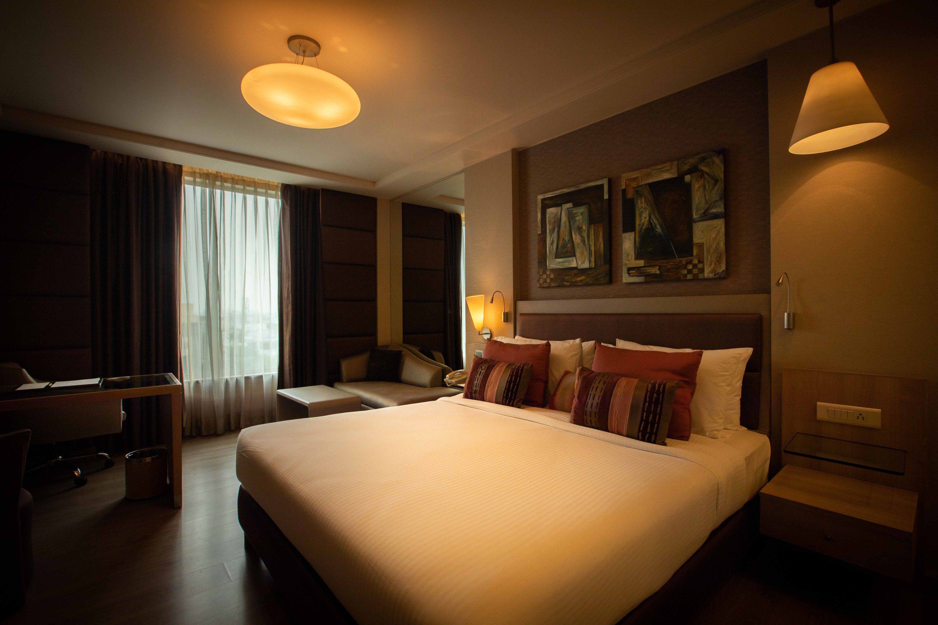 Habitación de hotel con una cama grande, un escritorio y una silla. Hay dos cuadros en la pared sobre la cama.