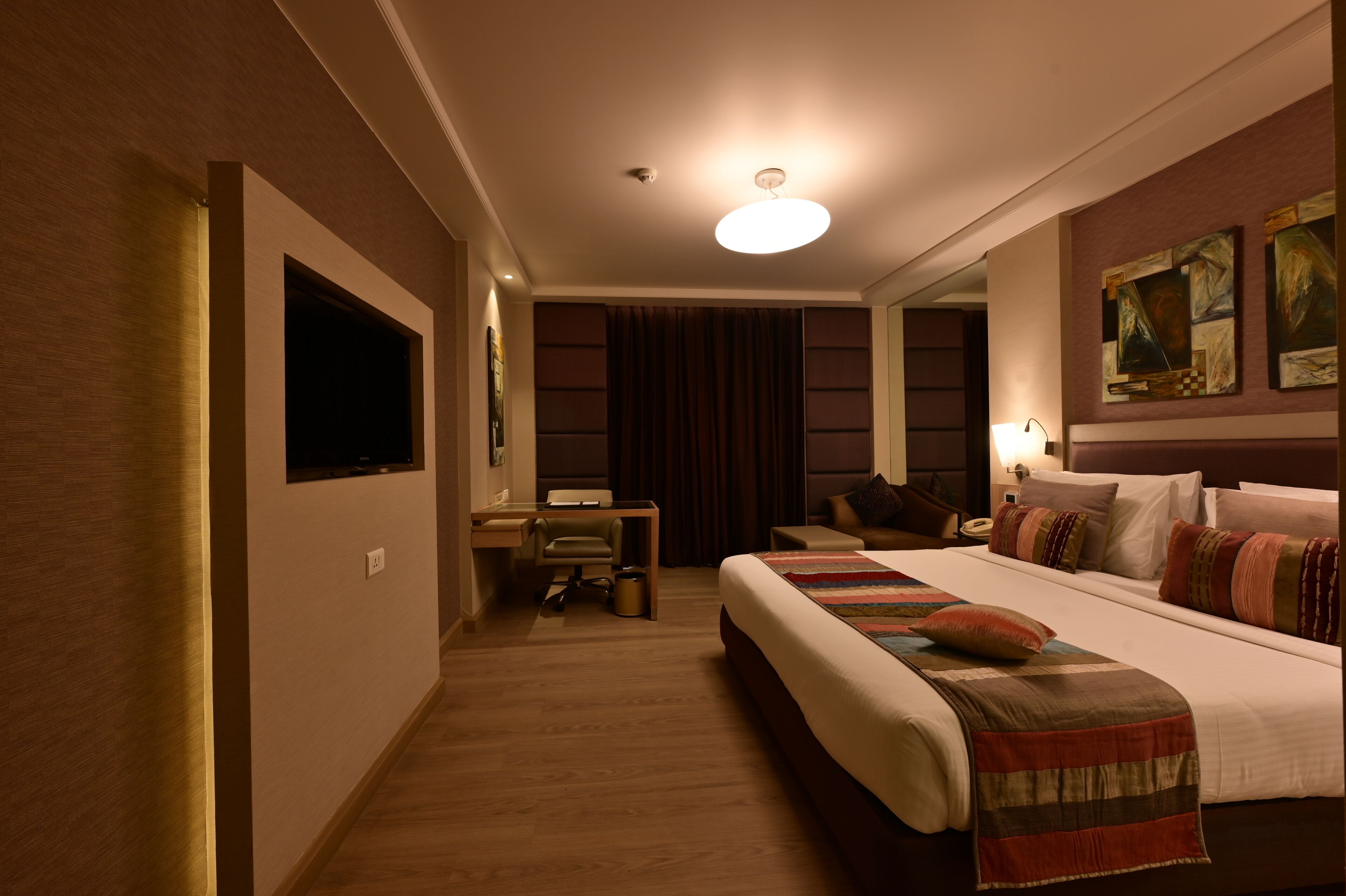 A hotel room with a large bed, a desk, a chair, and a television mounted on the wall.