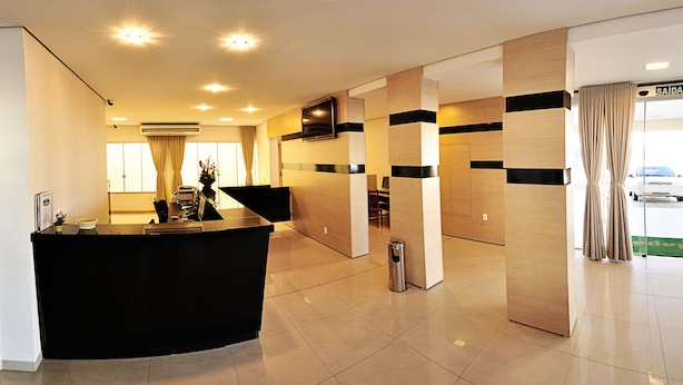 A hotel reception area with a black reception desk, a wall-mounted TV, and a sign reading "SAÍDA". - Jalapão Hotel (Palmas)
