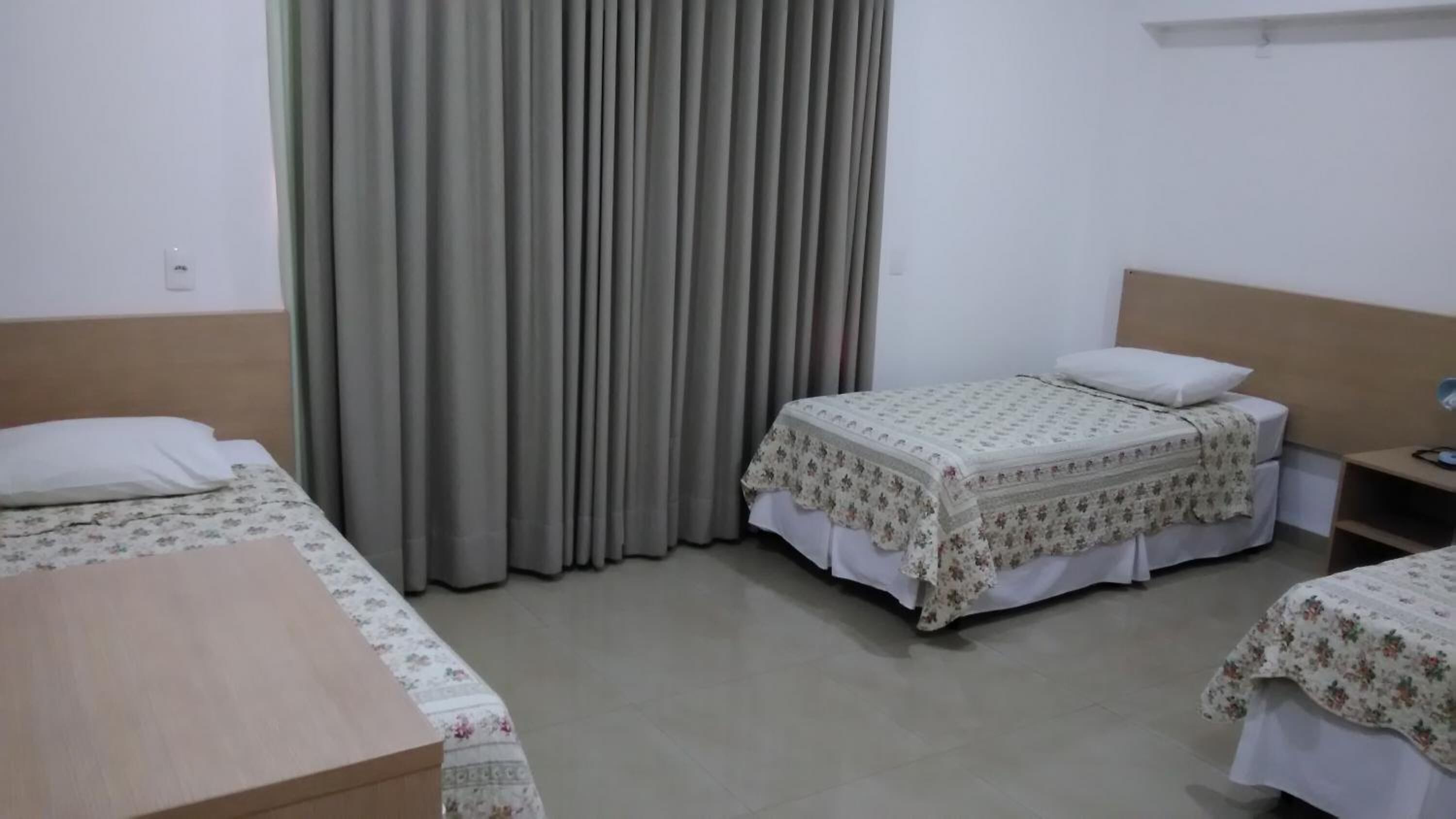 Habitación de hotel con dos camas individuales, un escritorio de madera, una mesita de noche y un ventanal con cortinas.