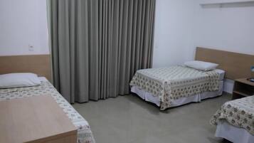 Habitación de hotel con dos camas individuales, un escritorio de madera, una mesita de noche y un ventanal con cortinas.