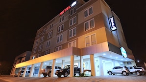 A hotel with a modern facade, multiple floors, and a covered parking area with several vehicles. - Jalapão Hotel (Palmas)