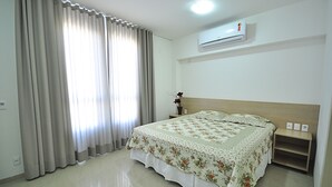 A bedroom with a bed, curtains, an air conditioner, and a nightstand. - Jalapão Hotel (Palmas)