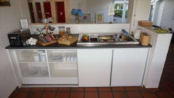 Una barra de desayuno con una máquina de café, pan, frutas y una variedad de acompañamientos.