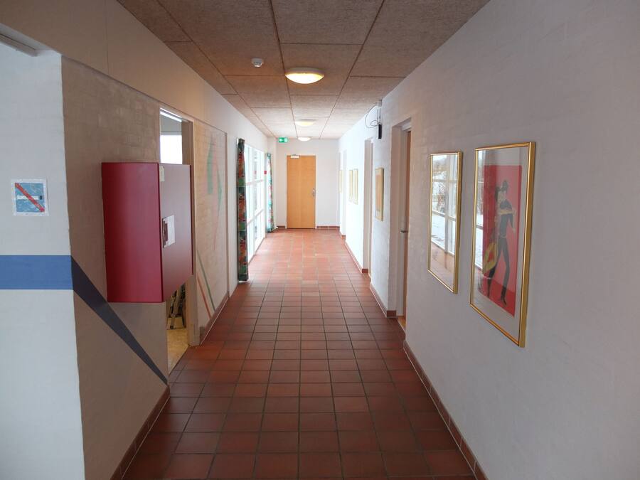 Ein langer Korridor mit Fliesenboden, weißen Wänden und gerahmten Kunstwerken.