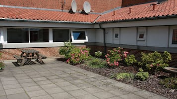 A courtyard with a brick building, satellite dishes, a picnic table, and flowering plants.
