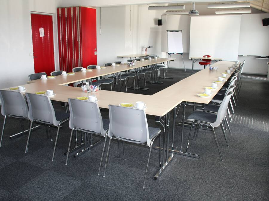 Un salón de conferencias con una mesa larga, sillas, una pizarra y una pantalla para proyector.