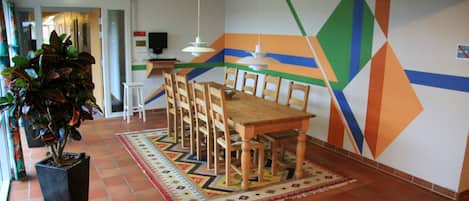 A conference room with a wooden table and chairs, a potted plant, and a colorful geometric wall design.