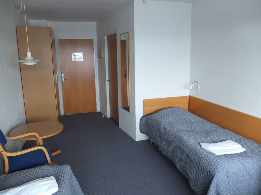 A hotel room with a single bed, a chair, a small table, and a wardrobe.