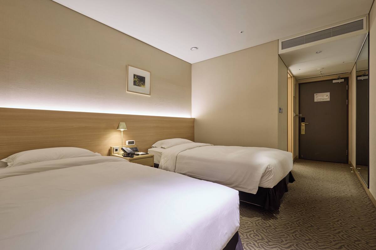 Une chambre d’hôtel avec deux lits, une table de chevet avec une lampe, un téléphone et une porte avec une pancarte.