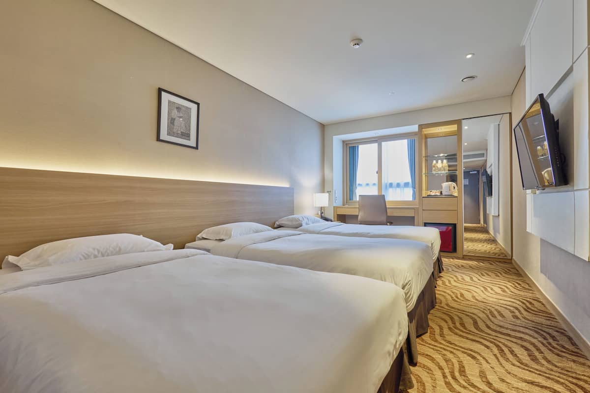 Une chambre d’hôtel avec trois lits, une grande fenêtre, un bureau et un téléviseur.