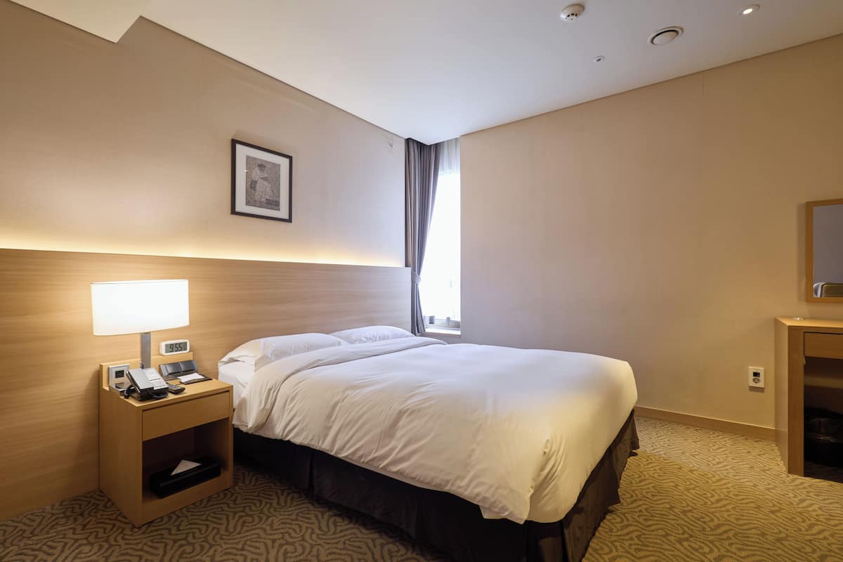 Une chambre d’hôtel avec un lit, une table de chevet avec une lampe, un téléphone et un petit tiroir.