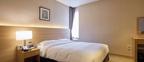 A hotel room with a bed, a nightstand with a lamp, a phone, and a small drawer.