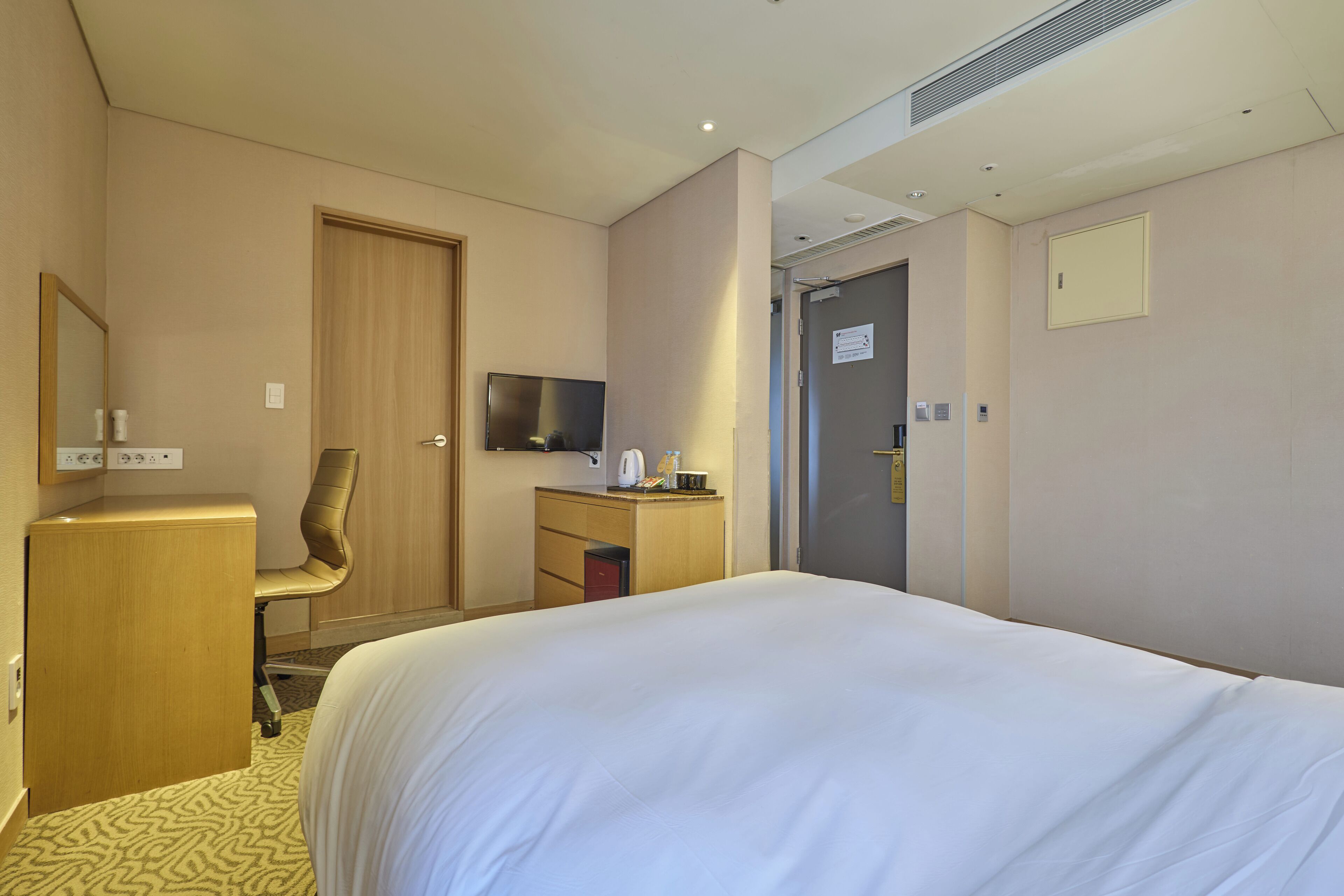 Ein Hotelzimmer mit Bett, Schreibtisch, Stuhl, Fernseher und einer Tür.