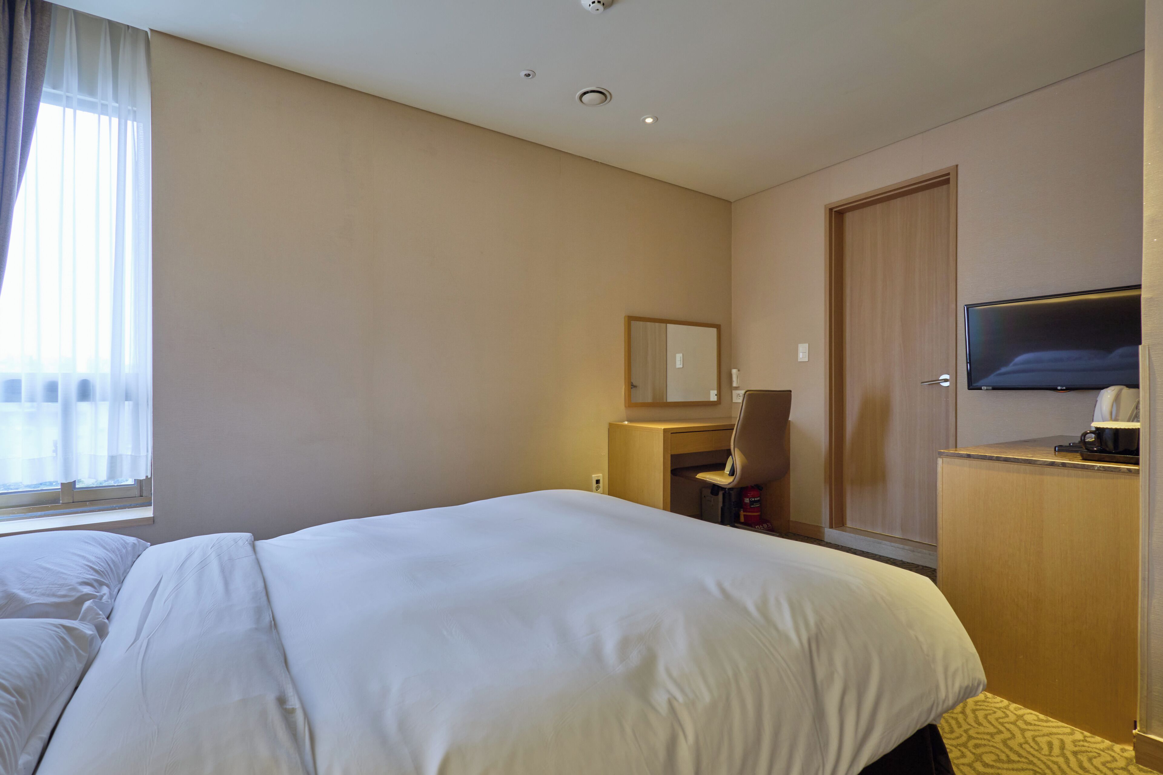 Ein Hotelzimmer mit einem großen Bett, einem Schreibtisch mit Stuhl, einem Fernseher und einem Kleiderschrank.