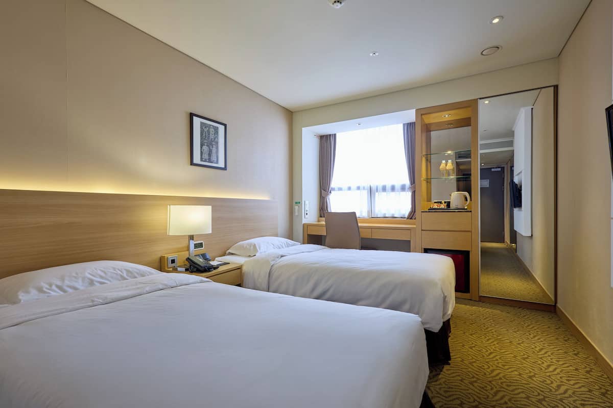 Une chambre d’hôtel avec deux lits, un bureau, une chaise, une lampe de bureau, un téléphone et une fenêtre avec des rideaux.