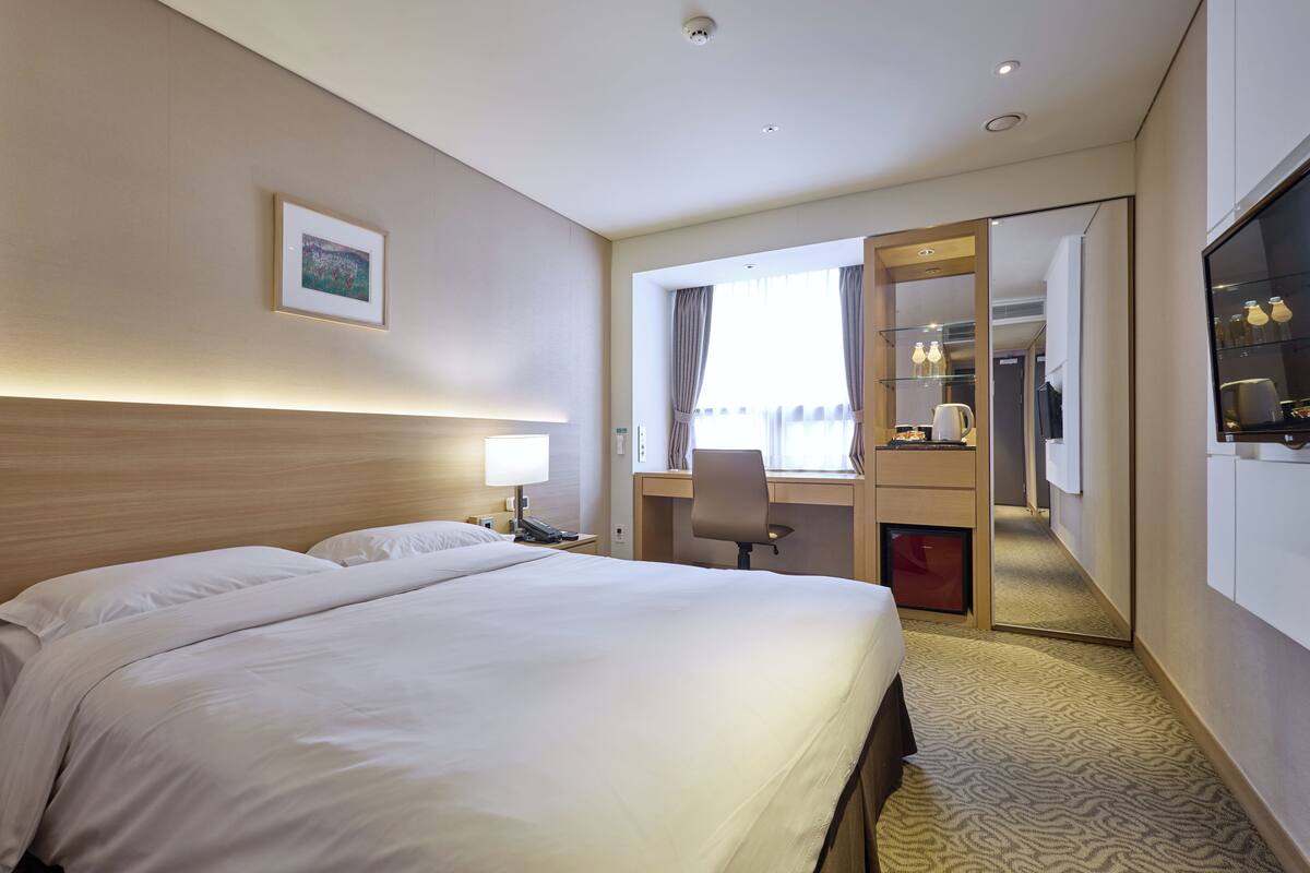 Une chambre d’hôtel avec un grand lit, un bureau avec une chaise, une télévision et une porte donnant sur un balcon.