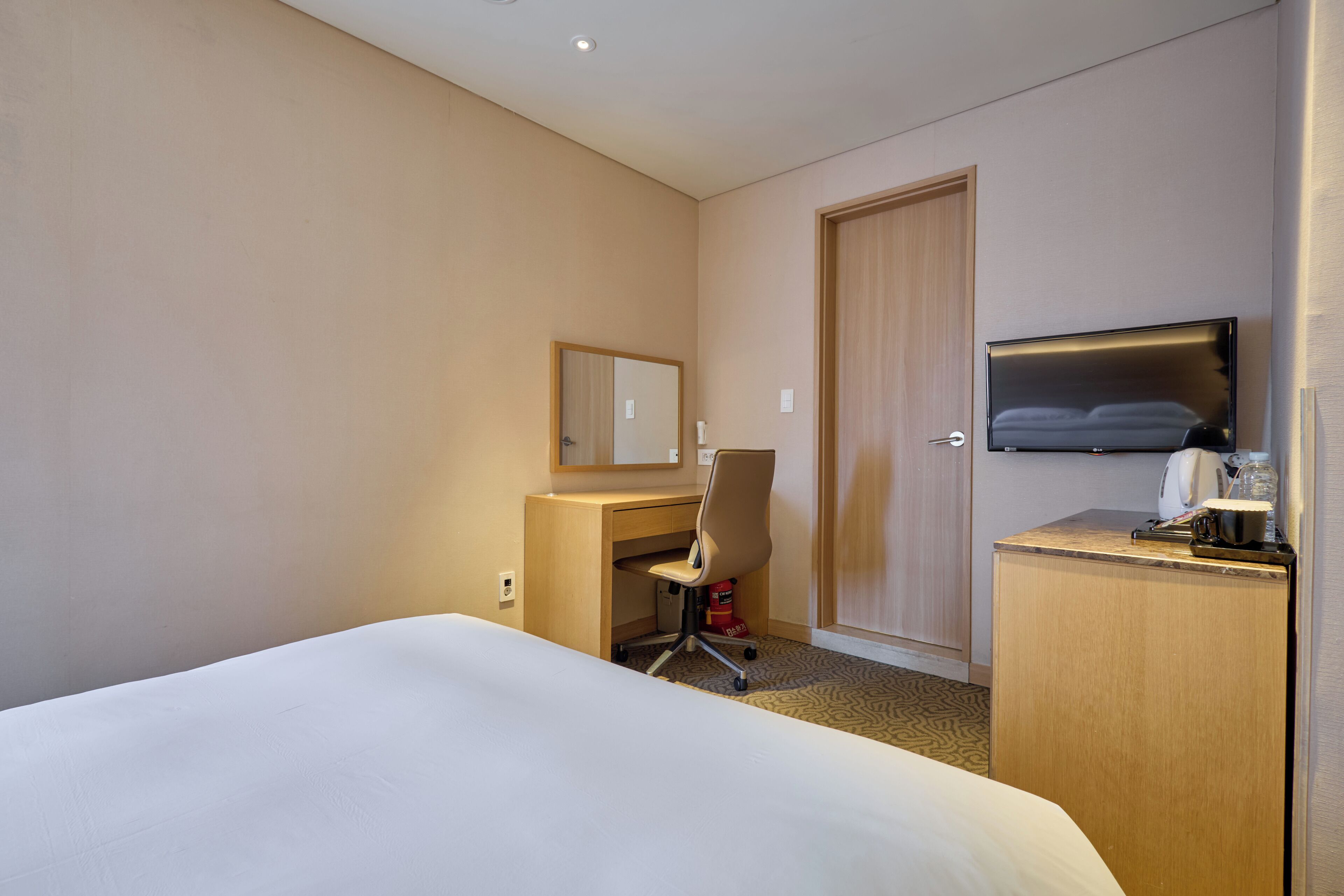 A hotel room with a bed, a desk, a chair, a television, and a door.