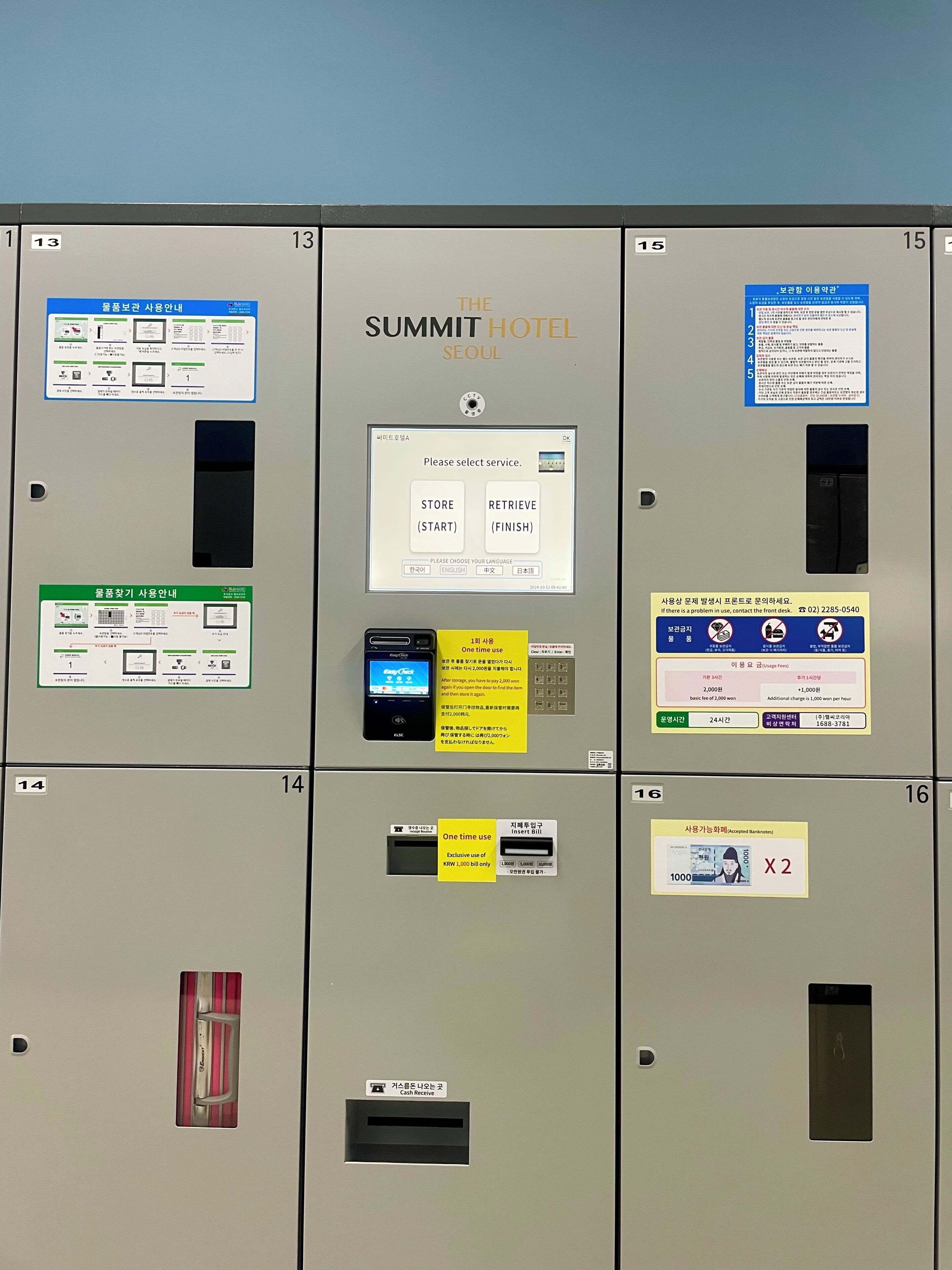 Eine Reihe von Hotelschließfächern mit verschiedenen Beschriftungen und Anweisungen, darunter ein Summit Hotel Schild und ein digitales Display zur Serviceauswahl.