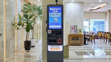 A WowPass self-service kiosk in a hotel lobby with a marble floor and a plant to the left.