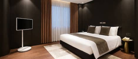 Una habitación de hotel moderna con una cama grande, una mesita de noche, un televisor de pantalla plana y un ventanal con cortinas.