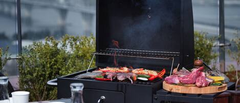 A barbecue grill with various meats and vegetables being cooked.
