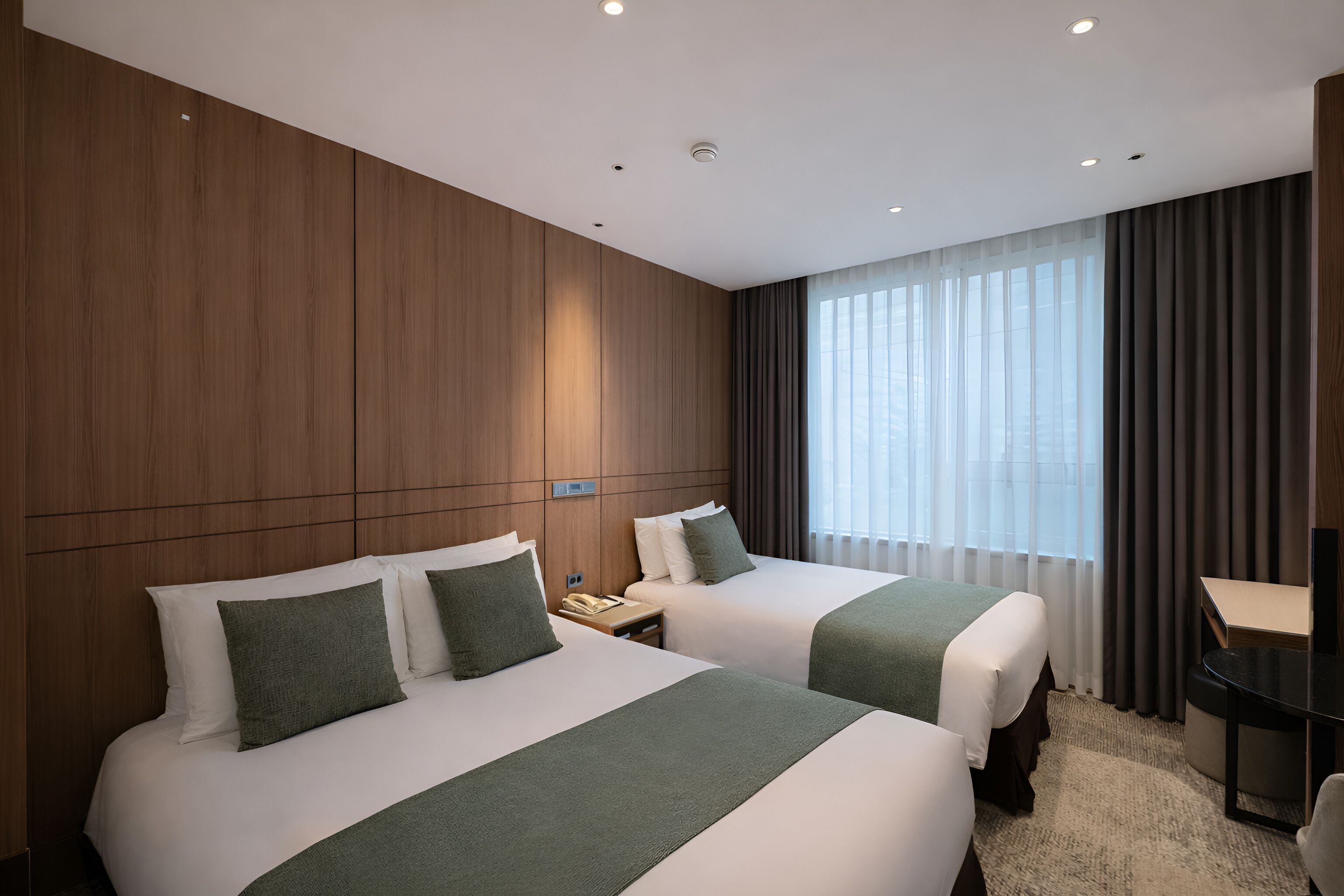 Habitación de hotel con dos camas, un escritorio y un ventanal grande con cortinas.