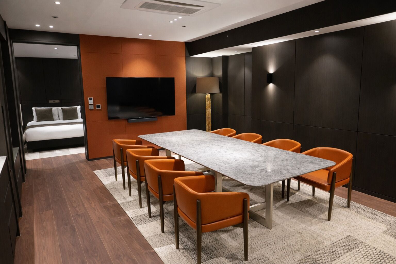 Una habitación de hotel moderna con una cama grande, televisión, mesa de comedor con sillas y zona de descanso separada.