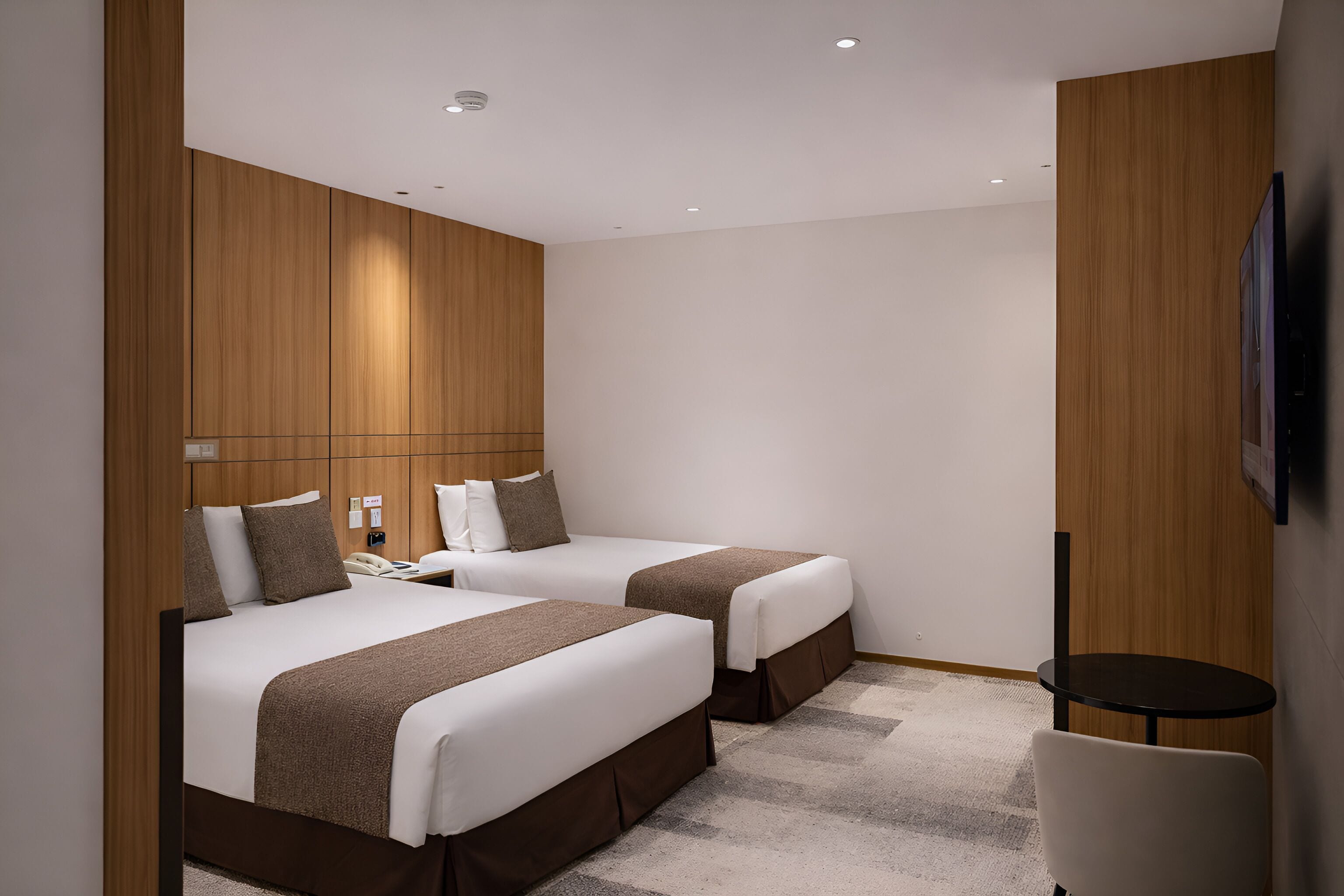 Habitación de hotel con dos camas, una mesita y un televisor montado en la pared.
