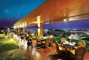 An outdoor dining area with tables and chairs, a view of a cityscape at night, and a covered section with a roof. - Golden Seoul Hotel (Seoul)