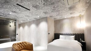 A modern hotel room with a large bed, a leather armchair, a round black table, and a shower area. - Hotel The Designers Jongno (Seoul)