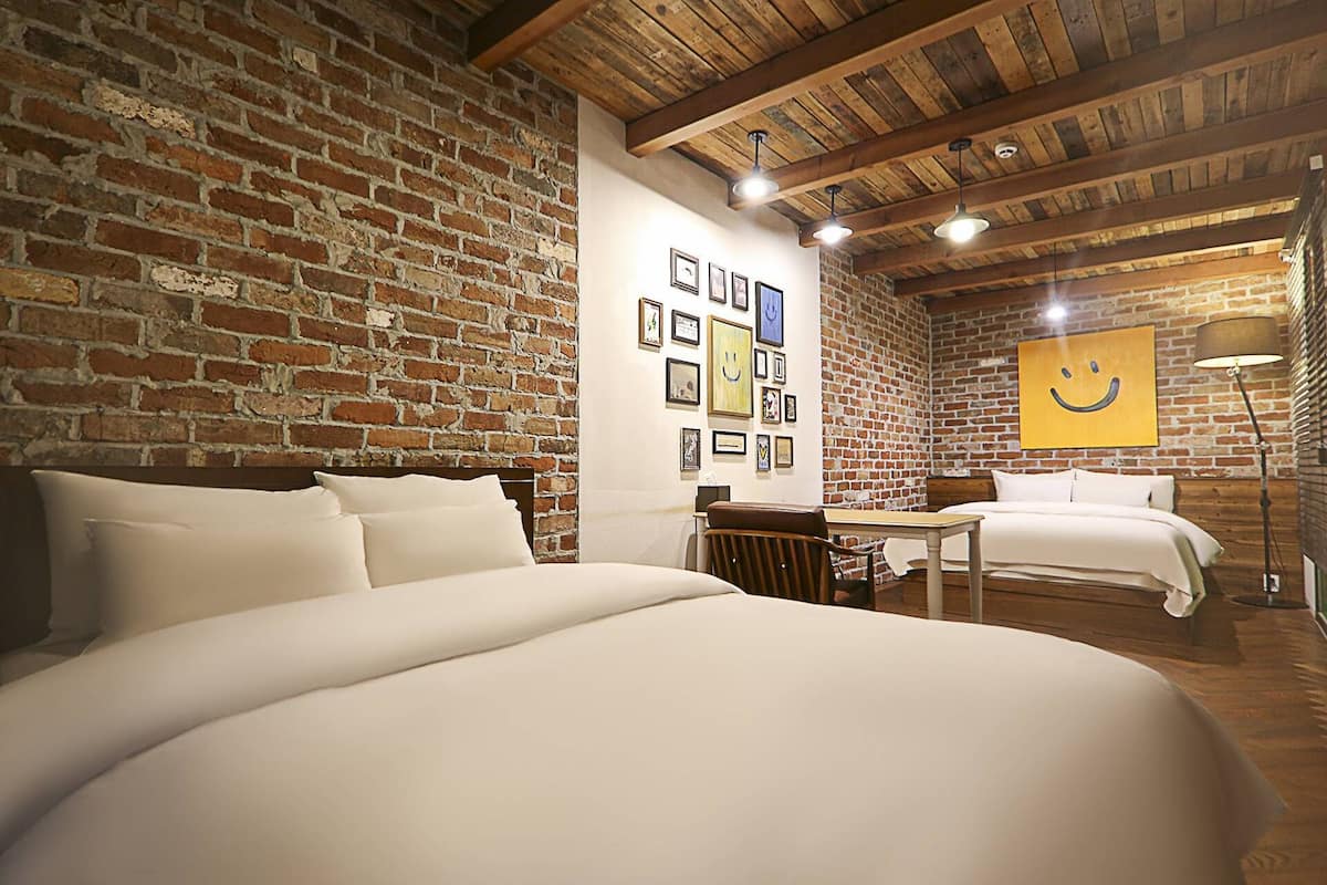 Una habitación con pared de ladrillo, una cama, un escritorio y una pared decorada con marcos.